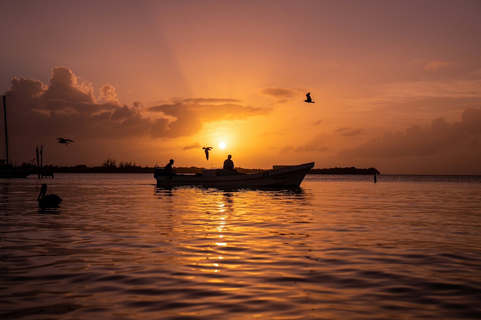Fishermen silhouetted in a boat at golden sunset on the water, Belize
