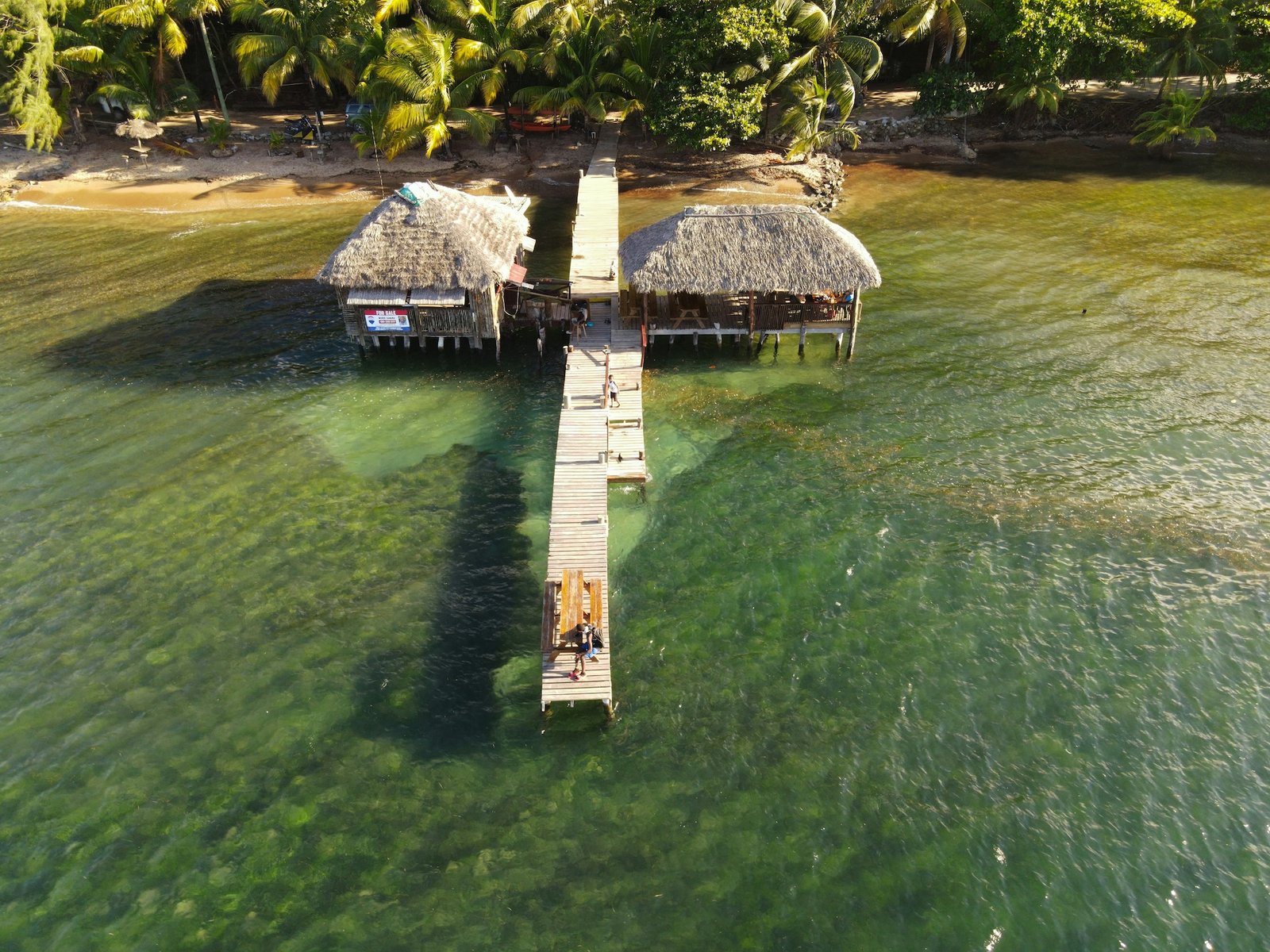 Overwater thatched-roof huts on a wooden dock above clear Caribbean water, Honduras